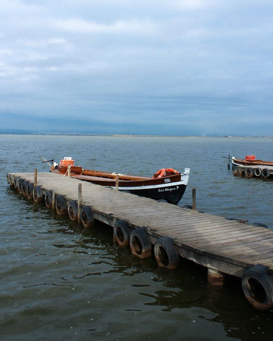 Barque traditionnelle en bois naviguant sur les eaux calmes du lac de l'Albufera près de Valence au coucher du soleil, avec des roseaux sur la rive