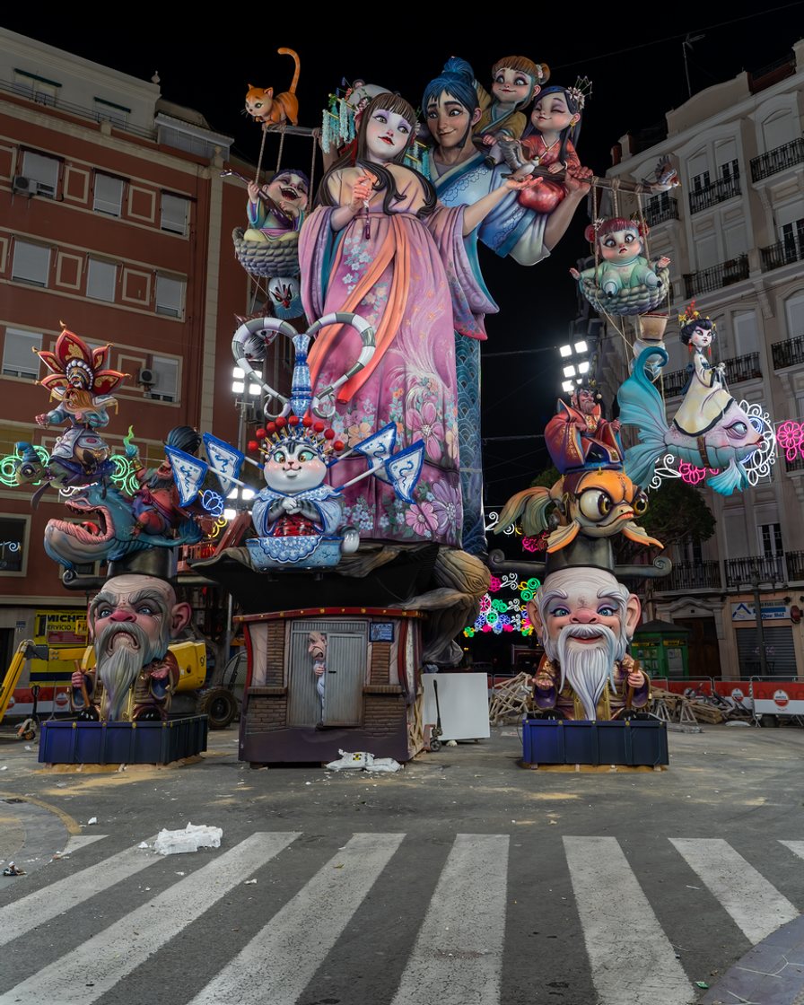 Falla monumental de Sección Especial de más de veinte metros en una plaza de Valencia, con figuras satíricas de colores y visitantes fotografiándola