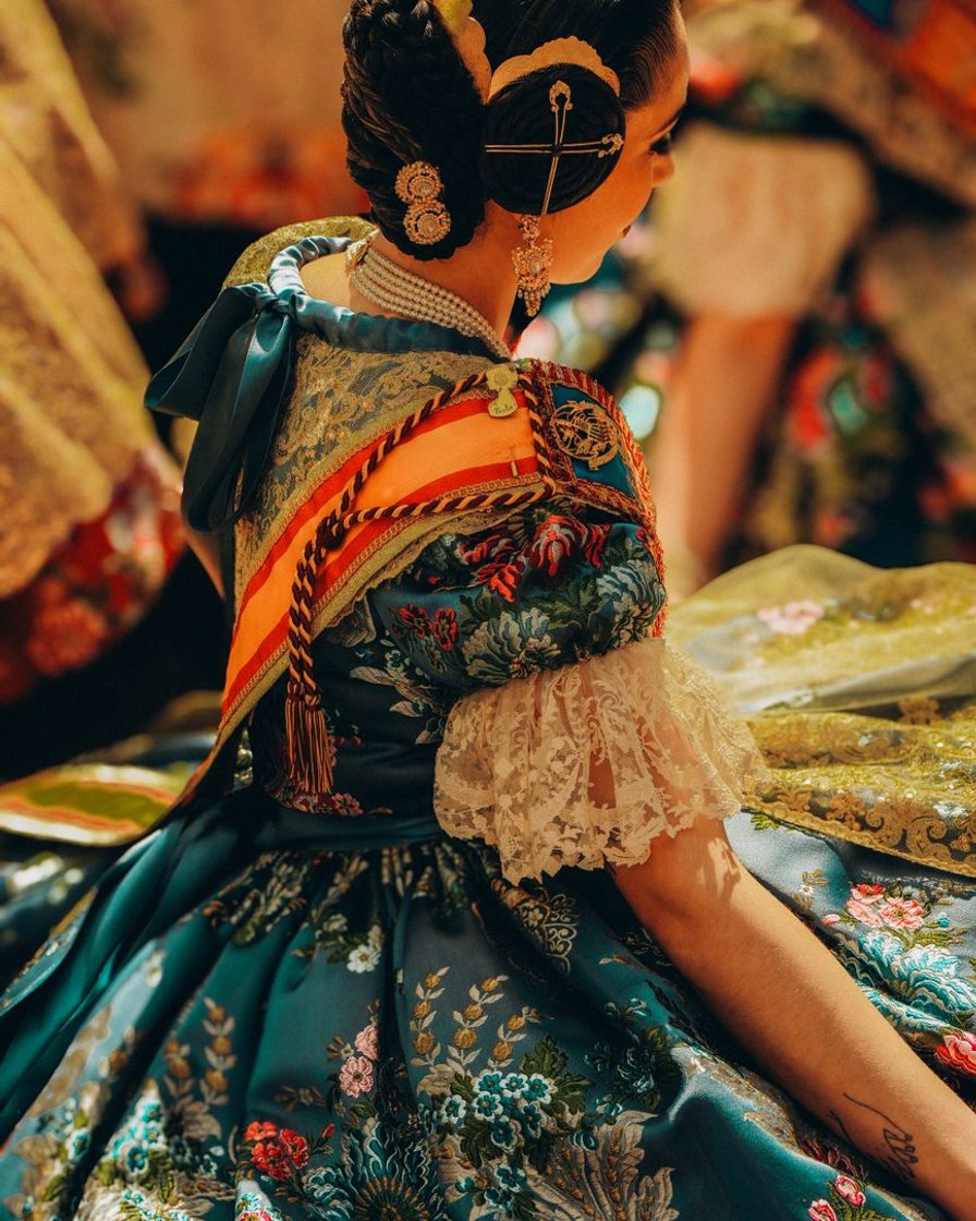 Grupo de falleras con peinetas, mantillas y trajes de seda bordada esperando su turno en una calle del centro de Valencia bajo el sol de la tarde