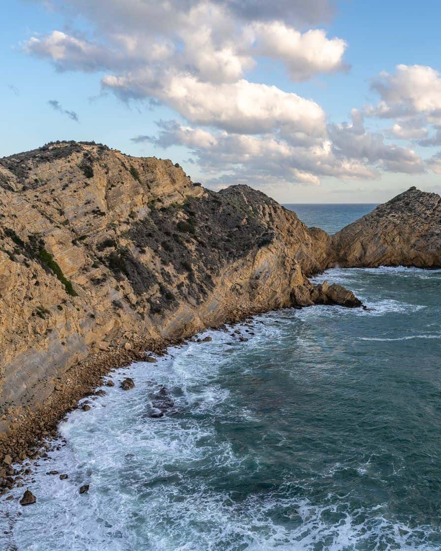 Crique aux eaux turquoise à Jávea, sur la Costa Blanca, avec des falaises rocheuses et une petite plage de sable vue depuis le rivage