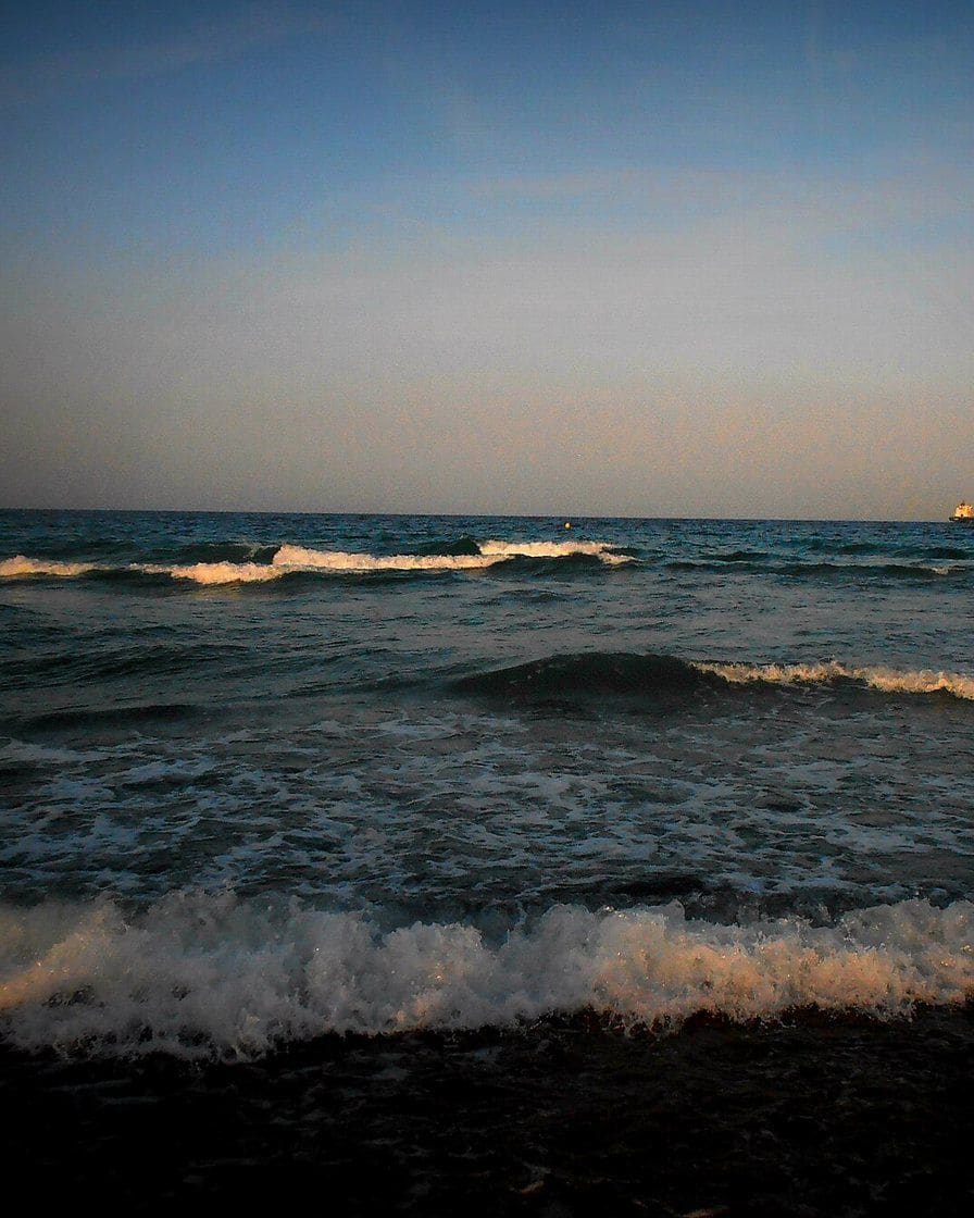 Playa de la Malvarrosa en Valencia al atardecer, con la arena dorada, el paseo marítimo y algunas personas paseando junto a la orilla