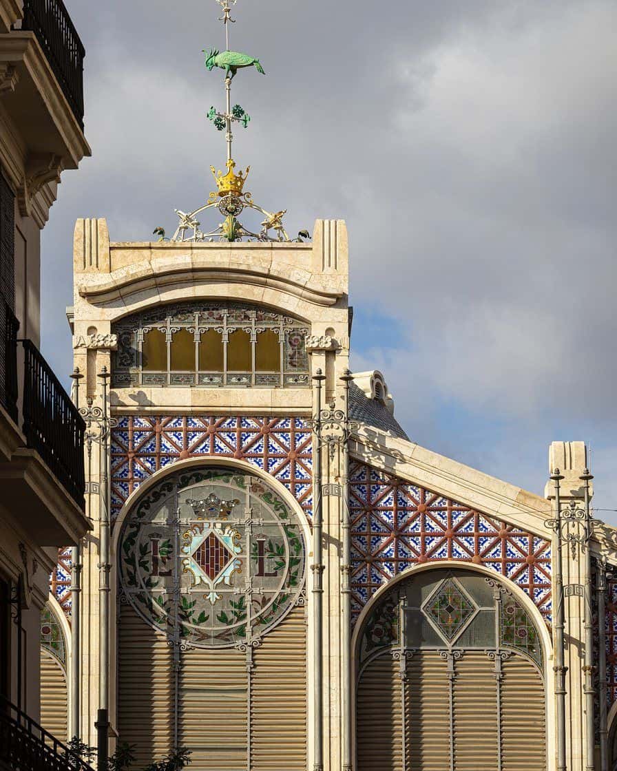 Fachada modernista de hierro forjado y cerámica del Mercado Central de Valencia vista desde la calle, con la cúpula acristalada destacando sobre la entrada principal