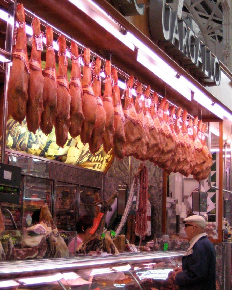 Fruit and vegetable stalls under the stained-glass dome of Valencia's Central Market, with customers shopping between the marble counters