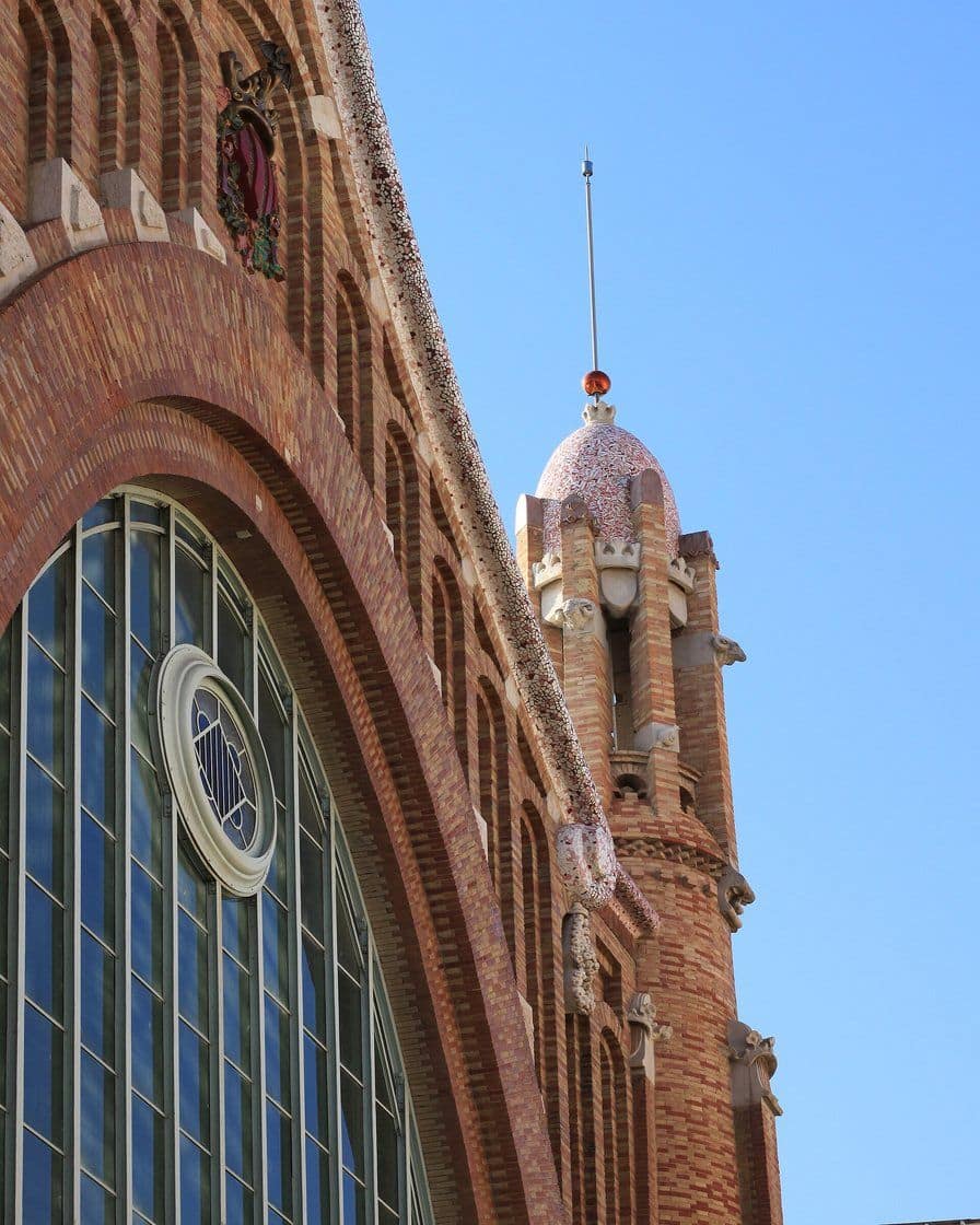 Fachada modernista de hierro y cristal del Mercado de Colón en Valencia, con terrazas activas en la planta baja durante un fin de semana soleado