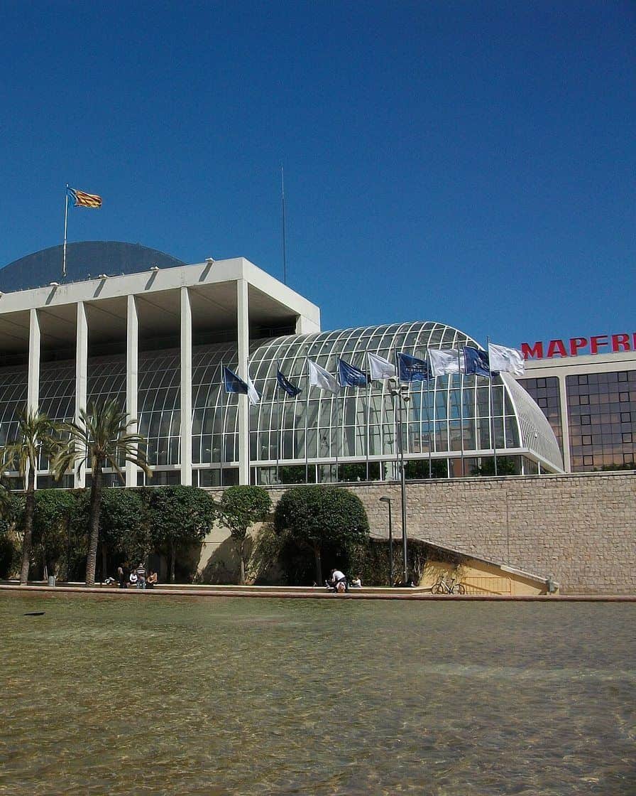 Fachada acristalada del Palau de la Música de Valencia junto a los jardines del Turia al atardecer, con el estanque delante