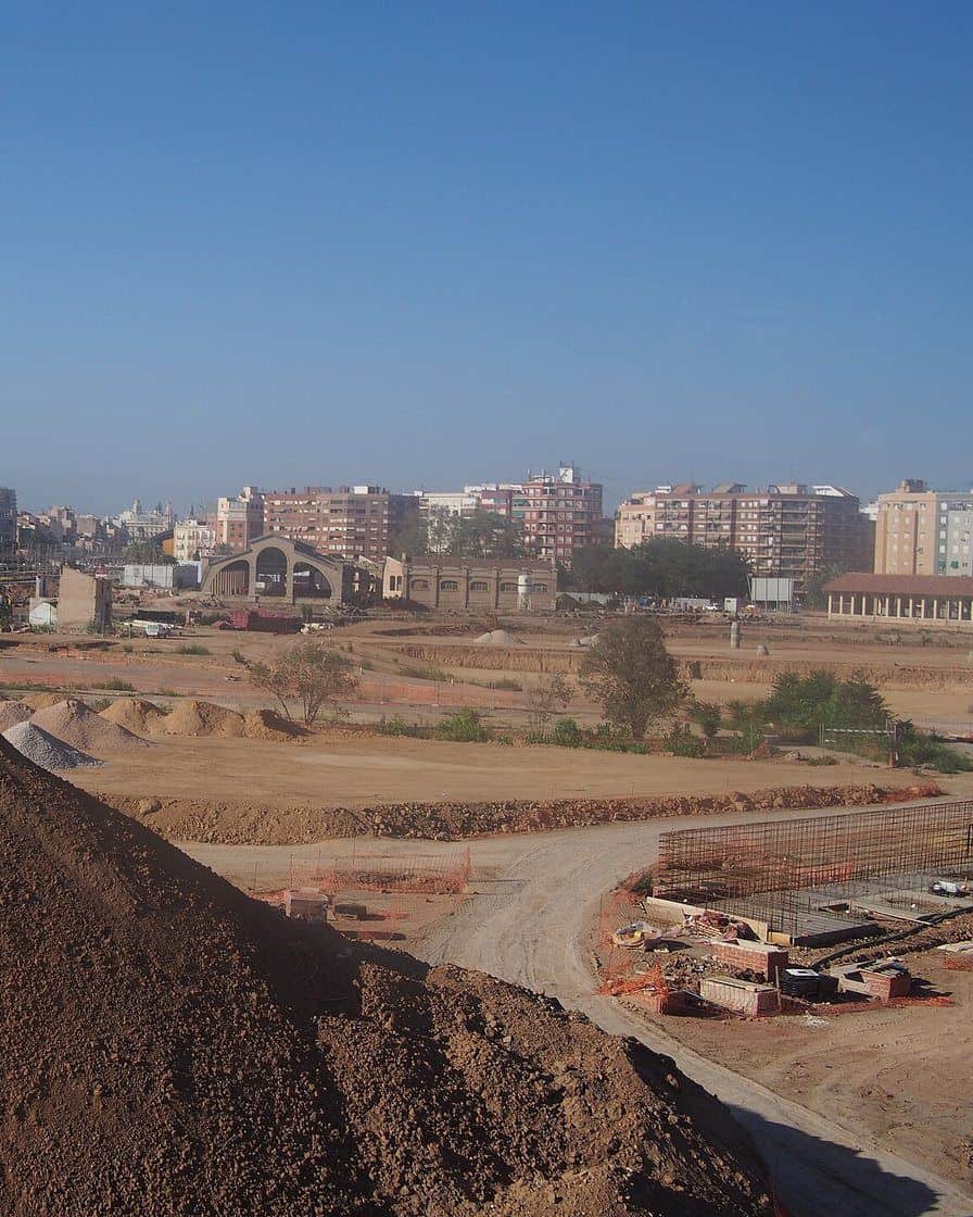Viale del Parque Central di Valencia accanto ai vecchi capannoni ferroviari restaurati, con prato, alberi giovani e famiglie a passeggio