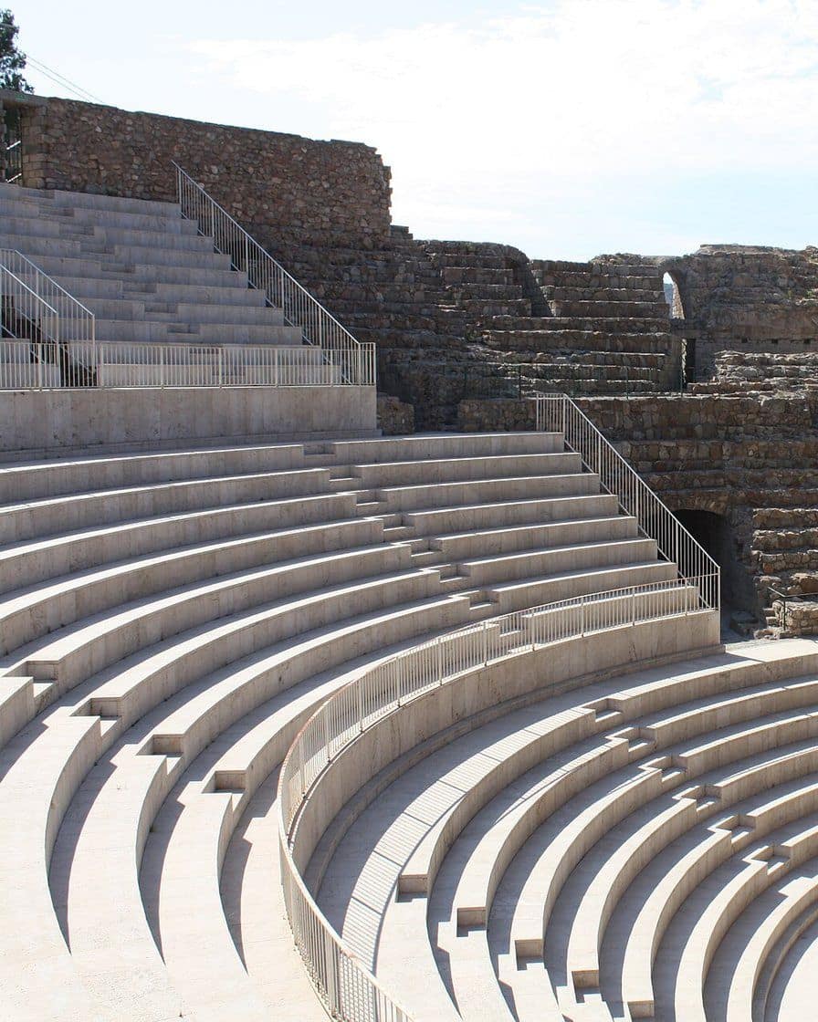 Teatro romano de Sagunto restaurado, con graderío de piedra en la ladera y el castillo en lo alto del cerro bajo un cielo azul